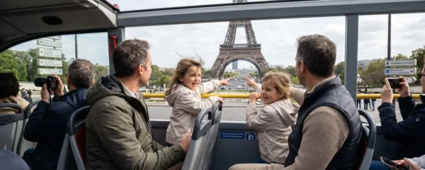 A family of four on the top deck of an open-air sightseeing bus in Paris, with children pointing towards the Eiffel Tower visible in the distance